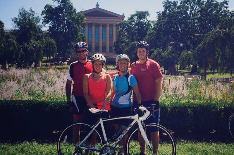 A family with a bike in biking clothes in front of the Philadelphia Museum of Art.